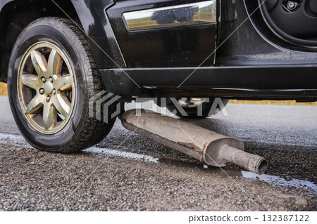 Broken exhaust pipe lying under a black car parked on the roadside after mechanical failure Broken exhaust pipe lying under a black car parked on the roadside after mechanical failure 132387122