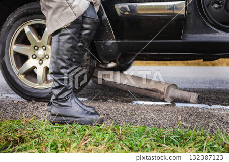Woman standing near a broken car with a fallen exhaust pipe on the roadside Woman standing near a broken car with a fallen exhaust pipe on the roadside 132387123