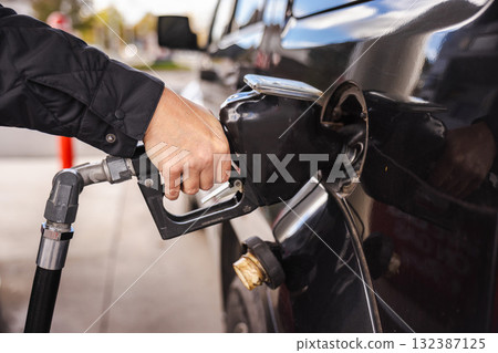 Person refueling a black car at a gas station, close-up of hand holding the fuel nozzle Person refueling a black car at a gas station, close-up of hand holding the fuel nozzle 132387125