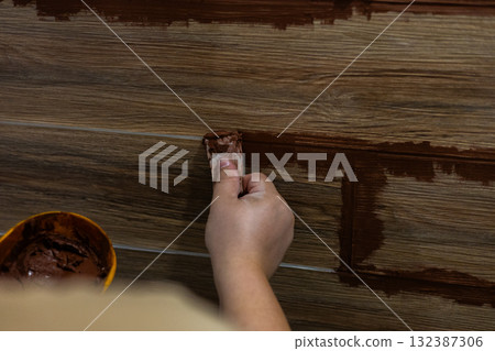 Hand-applying brown grout to the joints of ceramic floor tiles during a home renovation Close-up of a skilled craftsman or professional refinishing and refinishing flooring in a residential interior. 132387306