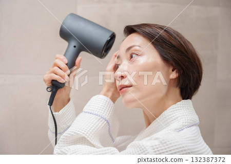 A woman using a hair dryer after taking a bath 132387372