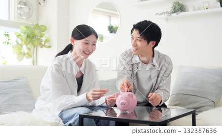 Asian couple putting money into a piggy bank Asian couple putting money into a piggy bank 132387636