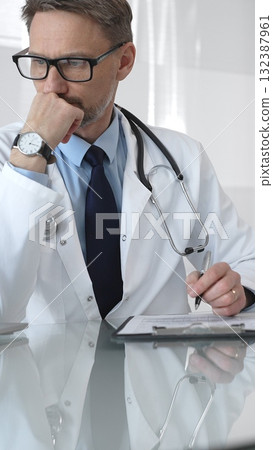 Male doctor in lab coat and stethoscope working on laptop, providing medical consultation in a modern clinic office. Medicine and health care Male doctor in lab coat and stethoscope working on laptop, providing medical consultation in a modern clinic office. Medicine and health care 132387961