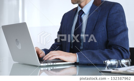 Professional businessman working on laptop computer, typing on keyboard at modern office desk, managing business tasks. Business people concept Professional businessman working on laptop computer, typing on keyboard at modern office desk, managing business tasks. Business people concept 132387962