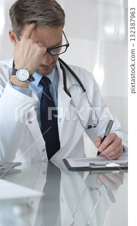 Male doctor in lab coat and stethoscope working on laptop, providing medical consultation in a modern clinic office. Medicine and health care Male doctor in lab coat and stethoscope working on laptop, providing medical consultation in a modern clinic office. Medicine and health care 132387963