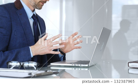 Businessman having a video conference, gesturing during an online business meeting or remote negotiation. Business people concept Businessman having a video conference, gesturing during an online business meeting or remote negotiation. Business people concept 132387965