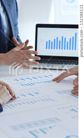 Business professionals collaborating at a table, discussing financial data and reports with a calculator and laptop displaying charts, focusing on strategy and planning Business professionals collaborating at a table, discussing financial data and reports with a calculator and laptop displaying charts, focusing on strategy and planning 132388115