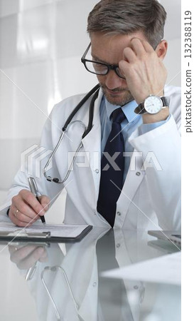 Male doctor in lab coat and stethoscope working on laptop, providing medical consultation in a modern clinic office. Medicine and health care 132388119