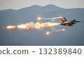 Military Jet Aircraft Releasing Flares During Flight Over Mountainous Terrain 132389840
