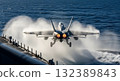 Military Jet Departing Aircraft Carrier on Blue Ocean Generating Vapor and Flames 132389843
