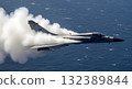 A Gray Fighter Jet Generating Vapor Trail Over Blue Ocean Depicting Speed and Power 132389844