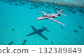 Aerial View Of A Gray Jet Plane Flying Over Turquoise Ocean With Shadow And Coral Reefs 132389849