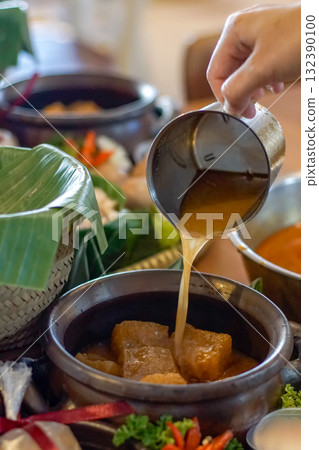 Indonesian krecek, a traditional spicy beef skin stew, with sauce being poured into a clay pot. Authentic Asian cuisine concept, perfect for themes of culinary culture, and traditional cooking 132390100