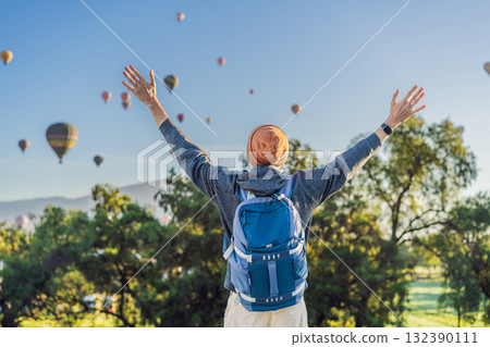 Male tourist standing with colorful hot air balloons floating in the sky behind him, enjoying adventure and sightseeing over Mexico. Travel, tourism, and exploration concept Male tourist standing with colorful hot air balloons floating in the sky behind him, enjoying adventure and sightseeing over Mexico. Travel, tourism, and exploration concept 132390111