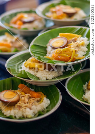 Several portions of authentic Indonesian food, Nasi Liwet or Nasi Ayam, white rice with shredded chicken, marinated egg, and vegetables served on banana leaf. Traditional Asian communal dining concept 132390582