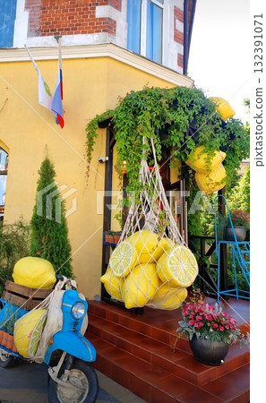 A sunny entrance to a yellow building, featuring a blue scooter and giant lemons as cheerful Mediterranean-style decor. 132391071
