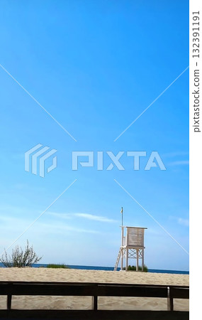 A tall, simple wooden lifeguard tower stands on the sandy beach against the deep blue sea. 132391191