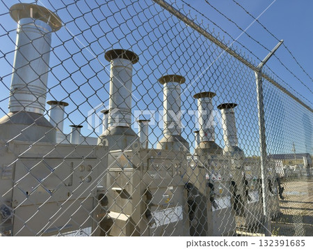 Industrial chimneys behind metal fence Industrial chimneys behind metal fence 132391685