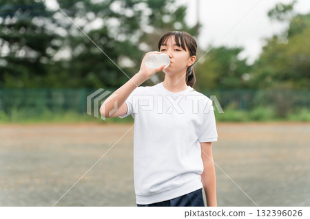 Female junior high and high school students in gym clothes hydrating while exercising on the school grounds Female junior high and high school students in gym clothes hydrating while exercising on the school grounds 132396026