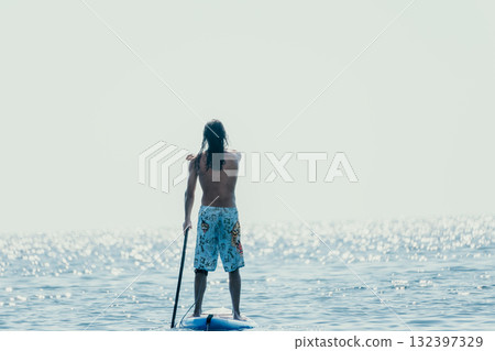 Man Sup Sea. Strong athletic man learns to paddle sup standing on board in open sea ocean on sunny day. Summer holiday vacation and travel concept. Aerial view. Slow motion 132397329