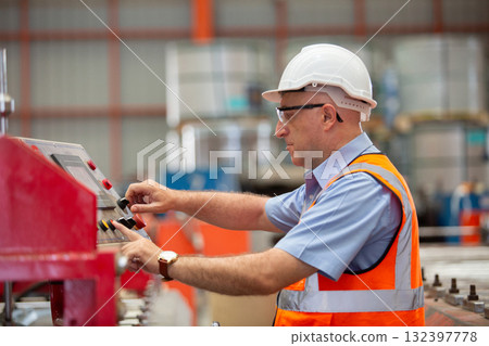 Factory technician wearing safety helmet and vest operating industrial machine control panel. Concept of automation, factory control system, machinery operation, and safety in manufacturing. 132397778