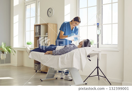 Male patient lying on couch in medical clinic and receiving IV drip infusion and vitamin therapy. 132399001