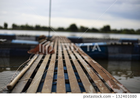 Walkway On Fish Cage By The Riverside, A sturdy walkway stretches over fish cages by the riverside, water shimmering below, perfect for a rustic photo or a vibrant visual display. Walkway On Fish Cage By The Riverside, A sturdy walkway stretches over fish cages by the riverside, water shimmering below, perfect for a rustic photo or a vibrant visual display. 132401080