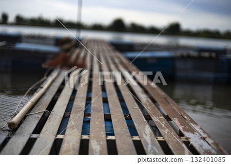 Walkway On Fish Cage By The Riverside, A sturdy walkway stretches over fish cages by the riverside, water shimmering below, perfect for a rustic photo or a vibrant visual display. Walkway On Fish Cage By The Riverside, A sturdy walkway stretches over fish cages by the riverside, water shimmering below, perfect for a rustic photo or a vibrant visual display. 132401085