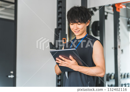 健身房裡的健身教練拿著平板電腦，年輕的男性私人教練 132402116