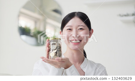 微笑的亞洲女人手裡拿著裝滿錢的罐子 微笑的亞洲女人手裡拿著裝滿錢的罐子 132403629