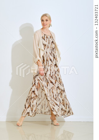 Elegant woman modeling a flowing patterned dress in a bright studio setting during daylight Elegant woman modeling a flowing patterned dress in a bright studio setting during daylight 132403721