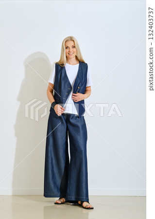 Stylish woman wearing a denim outfit poses for a fashion photo in a bright studio setting 132403737