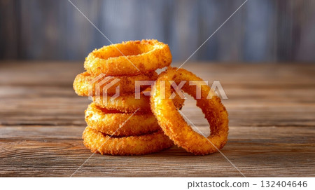 Crispy fried onion rings, golden brown, stacked on rustic wooden planks against a soft, blurred background 132404646