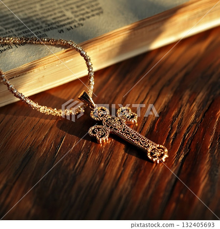 Gold cross necklace is on a wooden table next to a book Gold cross necklace is on a wooden table next to a book 132405693