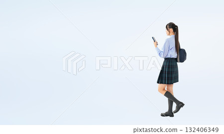 Full-body photo of a female student in uniform walking while looking at her smartphone Full-body photo of a female student in uniform walking while looking at her smartphone 132406349