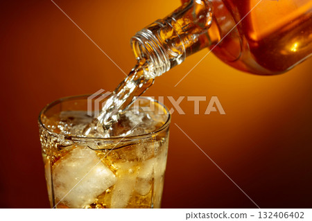 Bottle of whiskey pouring into a glass with ice. Bottle of whiskey pouring into a glass with ice. 132406402