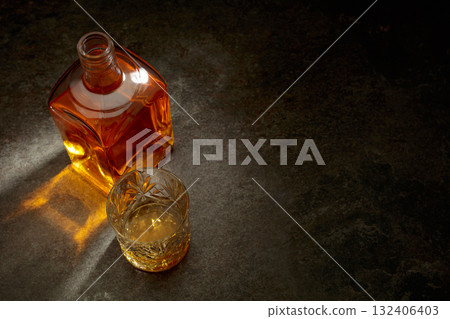 Bottle and crystal glass of whiskey on a stone table. Bottle and crystal glass of whiskey on a stone table. 132406403