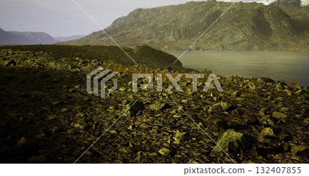 Rocky terrain leads to a serene lake surrounded by majestic mountains. The sun casts shadows on the landscape, highlighting the rugged beauty. Nature showcases its quiet elegance here. 132407855