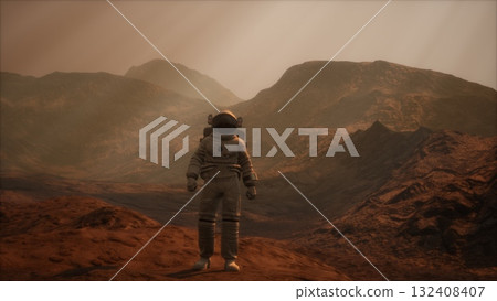 A lone astronaut stands on a rugged, reddish terrain, surrounded by towering mountains. The atmosphere is thin, creating a mysterious and otherworldly quality to the environment. 132408407