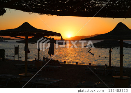 Sunrise over the sea against the backdrop of thatched umbrellas on the beach Sunrise over the sea against the backdrop of thatched umbrellas on the beach 132408523