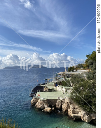 Coastal landscape with clear blue water and rocky shore under a bright cloudy sky Coastal landscape with clear blue water and rocky shore under a bright cloudy sky 132409006