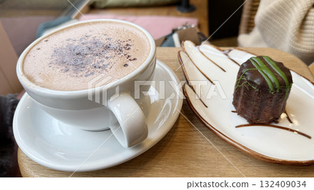 Cup of hot chocolate with cocoa powder and chocolate dessert on a plate, cozy cafe setting 132409034