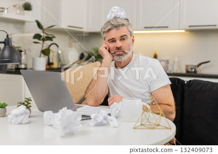 Middle-aged man writes ideas at table using laptop fights creative block tired unmotivated at home Middle-aged man writes ideas at table using laptop fights creative block tired unmotivated at home 132409073