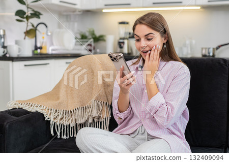 Young woman reacts wow eyes wide holding smartphone to positive big surprise and news about game win 132409094