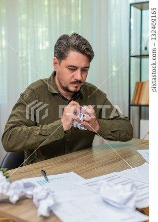 Middle-aged man crumples paper throws aside upset by report mistake frustrated angry at table desk 132409165