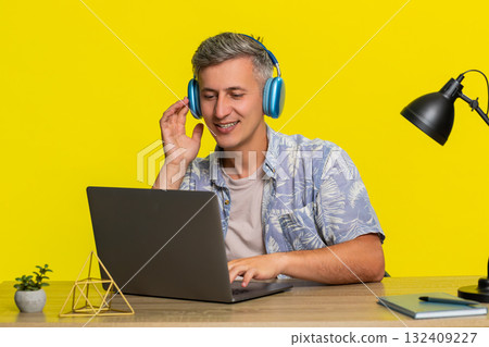 Man in wireless headphones working on laptop at table nodding head enjoying favorite music sound 132409227