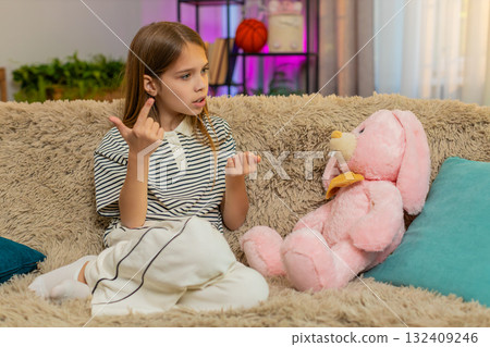 Child girl kid talking to plush bunny toy while sitting on home sofa in playful and imaginative mood Child girl kid talking to plush bunny toy while sitting on home sofa in playful and imaginative mood 132409246