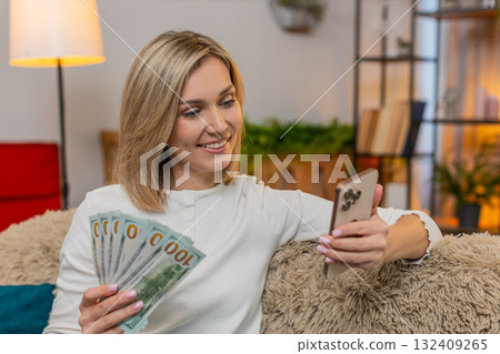 Woman counting money cash at home, using smartphone to plan family budget, calm confident expression 132409265