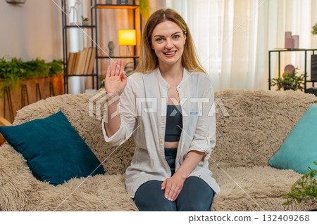 Adult woman smiling and waving hand hello at home, expressing greeting and happiness to see someone Adult woman smiling and waving hand hello at home, expressing greeting and happiness to see someone 132409268