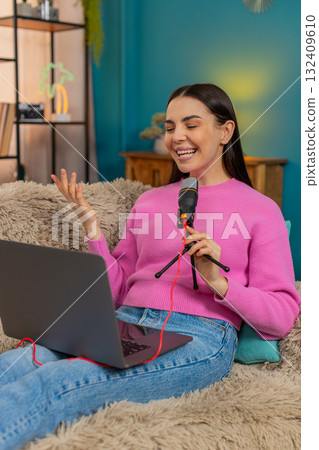 Young woman sitting on sofa recording podcast speaking seriously into microphone with focused look 132409610